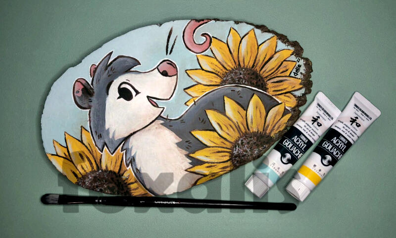 A photo of an acrylic painting on a wood slice of a smiling opossum surrounded by large sunflowers.